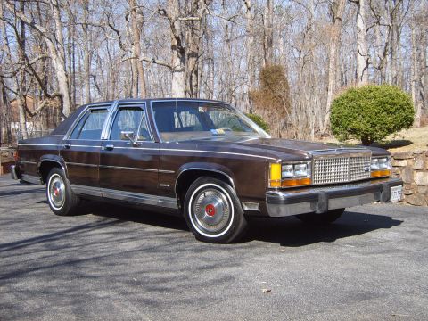 1982 Ford Crown Victoria LTD - This sedan features a distinctive grille and chrome accents, parked in a driveway with trees in the background.