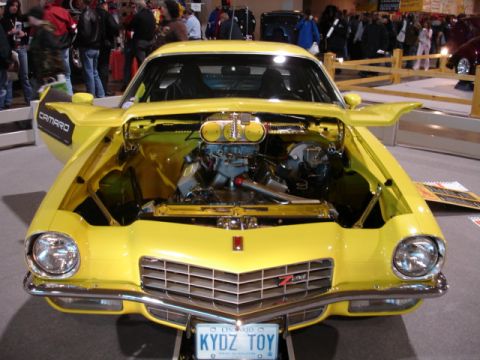 1981 Ford Mustang - A bright yellow Chevrolet Camaro is displayed with its hood open, revealing the engine and a "Camaro" decal on the fender.