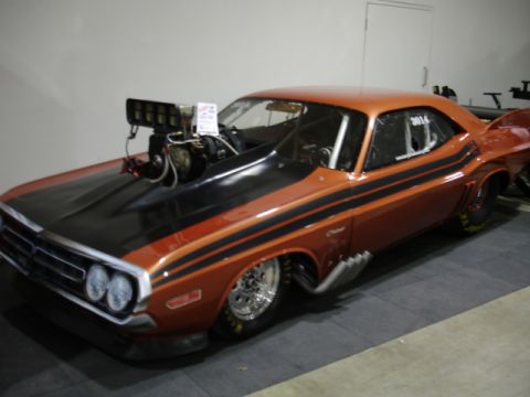 1981 Ford Mustang - This heavily modified orange drag car features prominent black stripes, a large hood scoop, and exposed side pipes.
