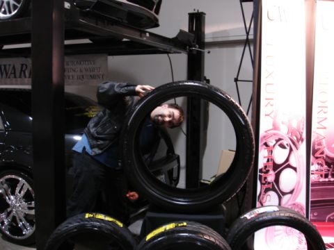 1981 Ford Mustang - A person peers through a large tire, with other tires and promotional displays visible in the background.