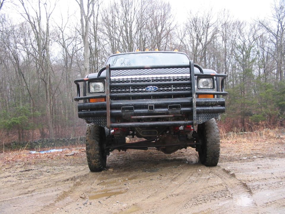 Lifted black Ford pickup with brush guard on muddy trail, front view
