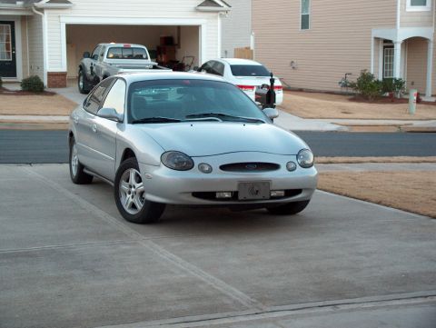 1998 Ford Taurus - This 1998 Ford Taurus is parked in a suburban driveway with a pickup truck and another car visible.