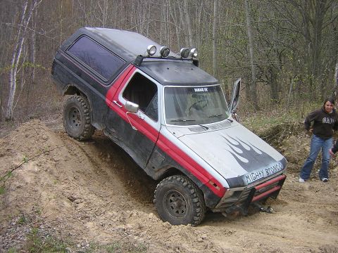1977 Ford F-150 - This modified Ford Bronco is tackling an off-road trail with its front wheels climbing a steep dirt embankment.