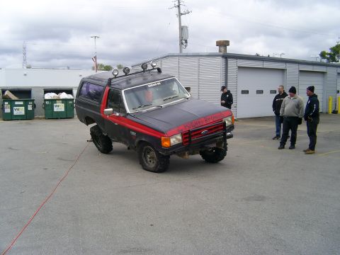 1977 Ford F-150 - A modified Ford Bronco II is parked in front of a commercial building with several people standing nearby.