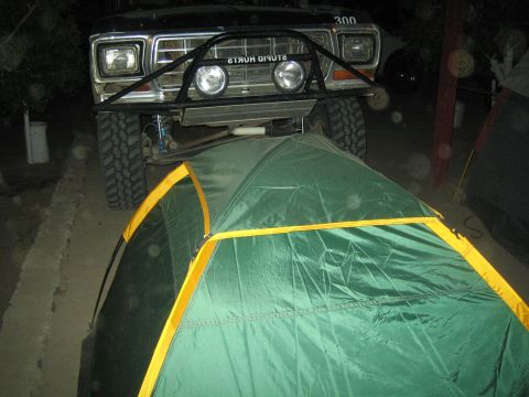 1990 Ford Bronco - Front of a lifted off-road truck, number 300, parked straddling a green dome tent at night.