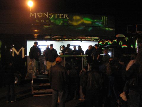 1990 Ford Bronco - crowd gathers at night around a lit Monster Energy promotional trailer with its branded logo overhead.