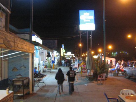 1990 Ford Bronco - nighttime street of shops and market stalls with a lit Corona sign and people walking down the sidewalk.