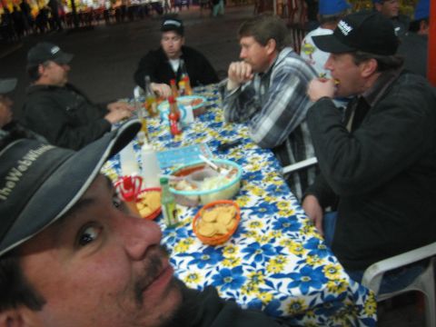 1990 Ford Bronco - group of men in caps and jackets eat chips and salsa around a long flower-patterned table indoors at night.