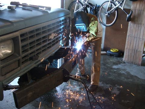 1990 Chevrolet Suburban - A person welds a custom bumper onto the front of a 1990 Chevrolet Suburban in a garage.