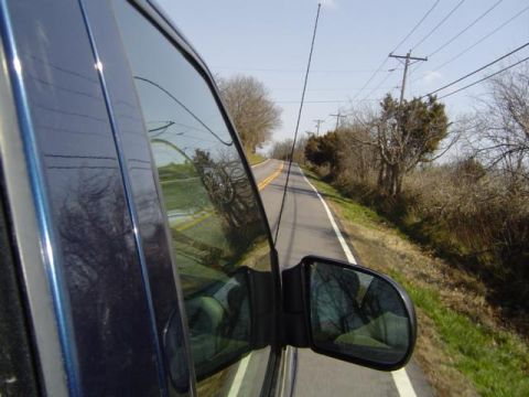 1979 Ford Bronco - Driving down a two-lane road with trees and power lines visible from the car window.
