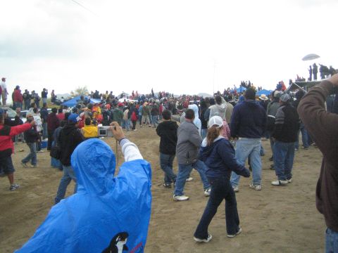 1990 Ford Bronco - large crowd in jackets and rain ponchos gathers on a dusty hillside under an overcast sky at an outdoor event.