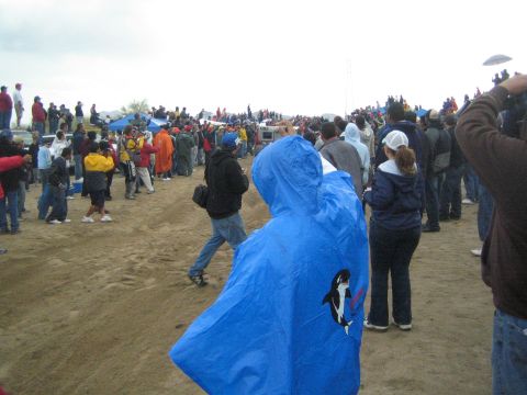 1990 Ford Bronco - crowd of spectators stands on a dusty open field, with one person wearing a blue orca-printed rain poncho.