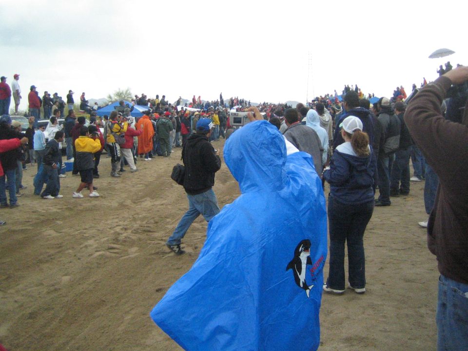 Crowd of spectators with a person in a blue orca poncho on a dusty open field