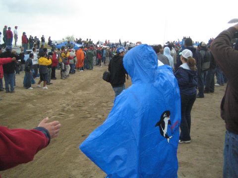 1990 Ford Bronco - Spectators stand watching on a dusty field under an overcast sky, with one wearing a blue orca-printed poncho.