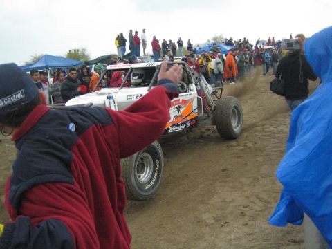 1990 Ford Bronco - orange and white off-road race buggy marked 22 with BFGoodrich tires drives along a dirt course as spectators wave it on.