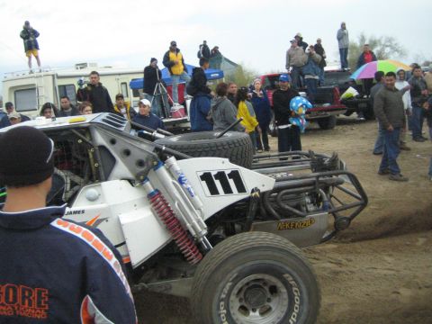 1990 Ford Bronco - rear of off-road race buggy number 111 shows its exposed roll cage, coilover shocks and McKenzie components amid a crowd of spectators.