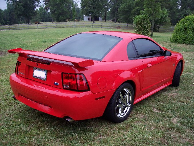 Red New Edge Ford Mustang coupe with rear spoiler and chrome wheels, three-quarter rear view on grass