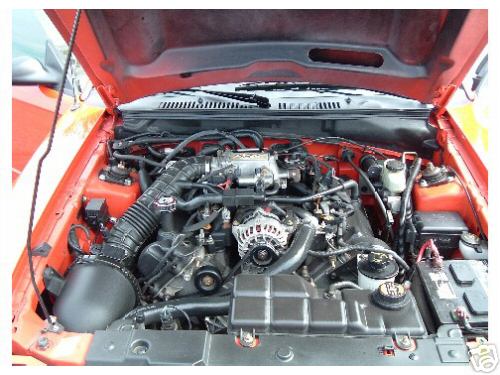 Engine bay of red car with black intake, alternator and battery visible