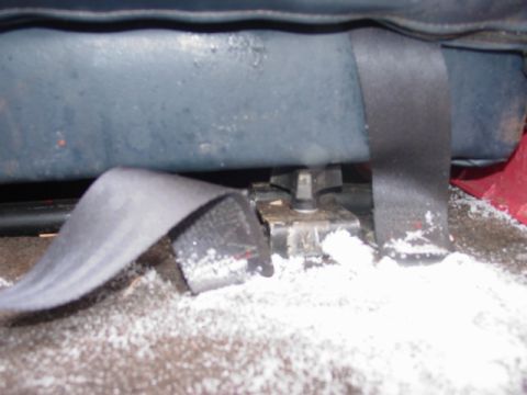 1986 Ford Bronco - Close-up of a seatbelt buckle and its mounting hardware on the vehicle floor, covered in white debris.