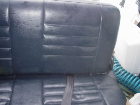 1986 Ford Bronco - The interior of a vehicle shows dark blue vinyl seats with a seatbelt in place.
