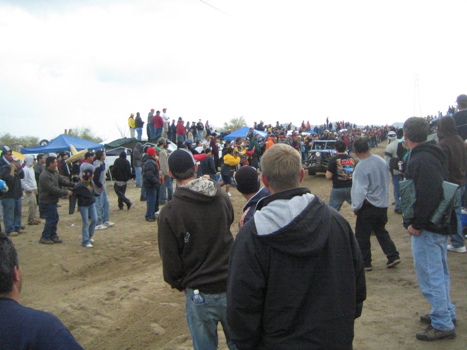 Spectators lining a dirt course with a race vehicle in the distance
