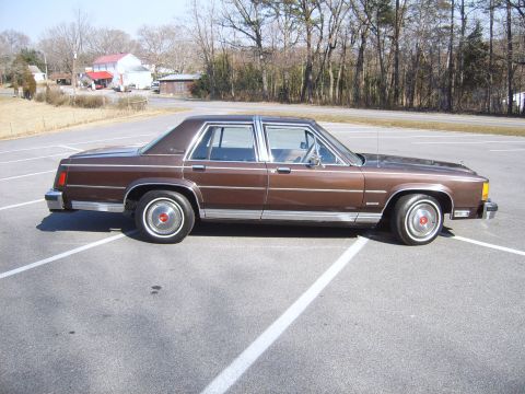 1982 Ford Crown Victoria LTD - A brown sedan is parked in a lot with trees in the background.