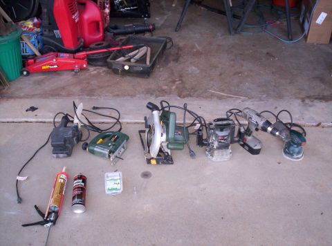 1995 Ford Bronco - Various power tools and a car jack are laid out on a concrete floor in a garage.