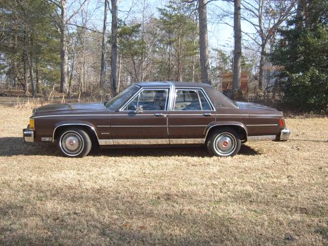 1982 Ford Crown Victoria LTD - A brown sedan sits in a grassy, wooded area on a clear day.