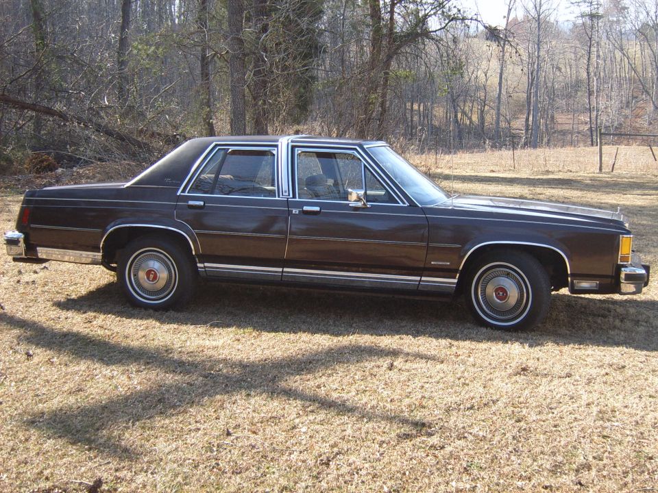 1982 Ford Crown Victoria LTD sedan, side view, parked on dry grass with trees in background