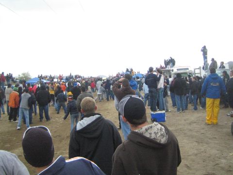 1990 Ford Bronco - Spectators in cold-weather clothing spread across a dirt field watching an event, with canopy tents and an RV in the background.