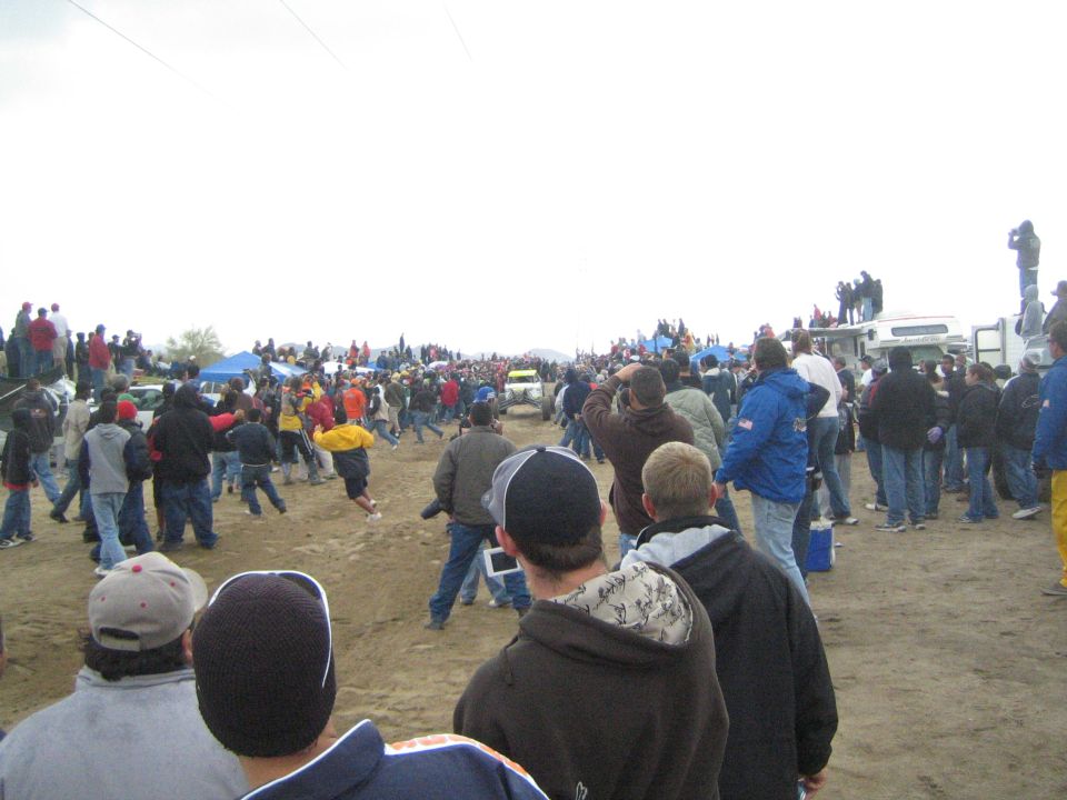 Crowd of spectators in jackets and caps lining a dirt course at an off-road desert race