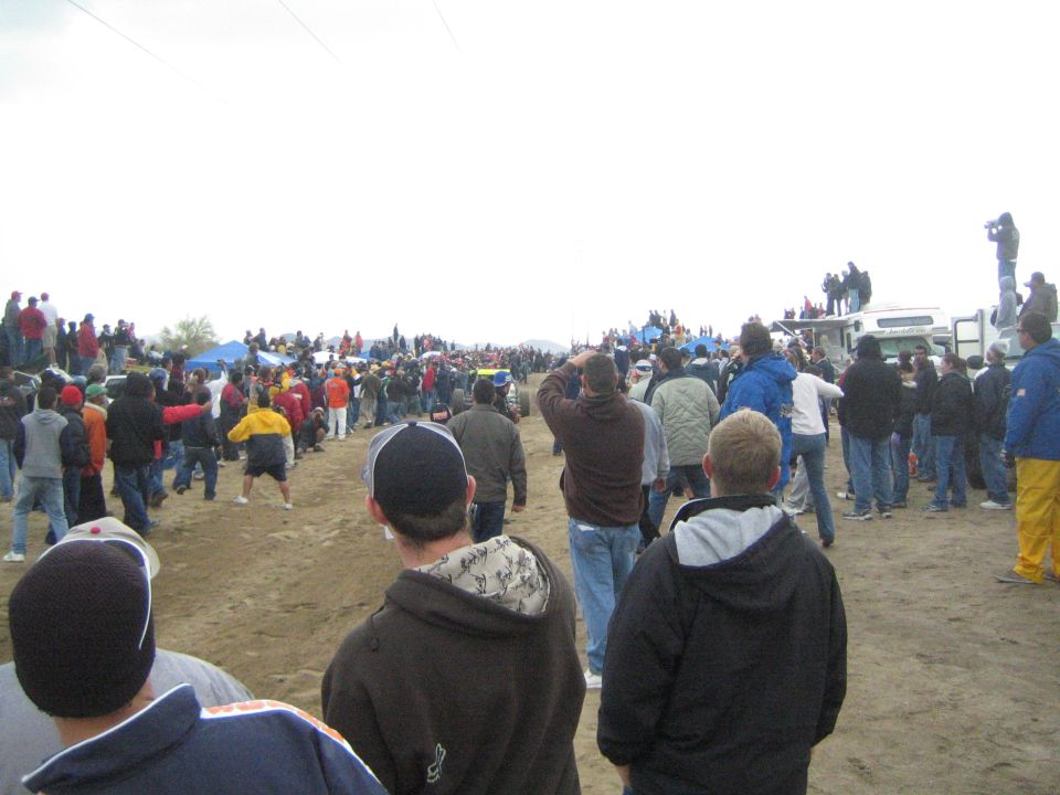 Spectators in hoodies and caps watching from a dirt course at a desert race