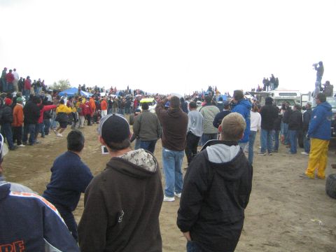 1990 Ford Bronco - Spectators line a dirt course at an off-road race; one foreground jacket reads SCORE International Off Road Racing.