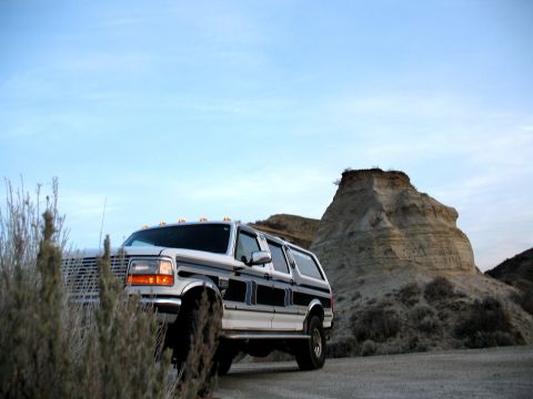 1994 Ford C-350 (Centurion Conversions) - A white Ford SUV is parked on a dirt road with a large rock formation behind it.