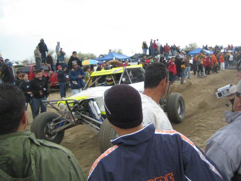 1990 Ford Bronco - white and yellow open-wheel off-road race buggy marked 66 navigates a sandy course as spectators watch closely.
