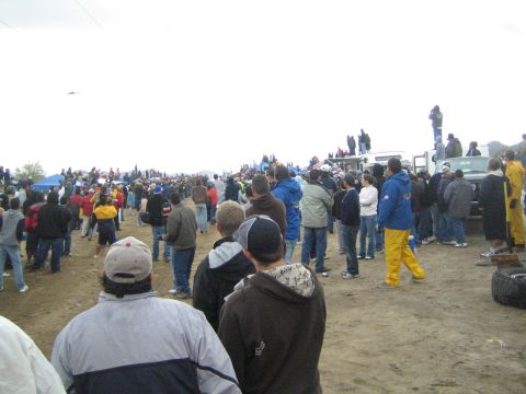 1990 Ford Bronco - Spectators crowd a dirt course, several standing atop a pickup truck for a better view of an off-road desert race.