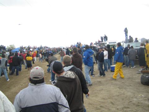 1990 Ford Bronco - large crowd lines a dirt off-road course while several people stand on a white truck to watch the race.
