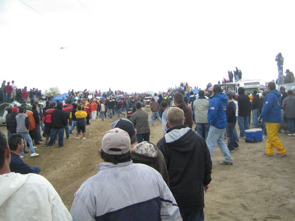 Spectators on a dirt course under gray sky at an off-road desert race