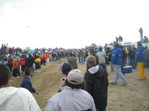 1990 Ford Bronco - dense line of spectators stretches along a dirt off-road course, with people perched on a truck and tents in the distance.