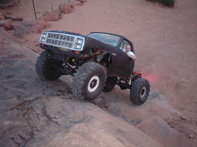 Black modified truck with oversized tires climbing a rocky incline