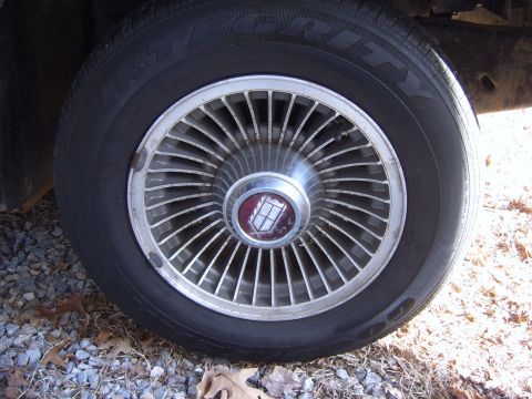 1982 Ford LTD Crown Victoria - Close-up of a turbine-style wire-look wheel cover with a chrome center cap and maroon emblem, mounted on a Goodyear Integrity whitewall-let…