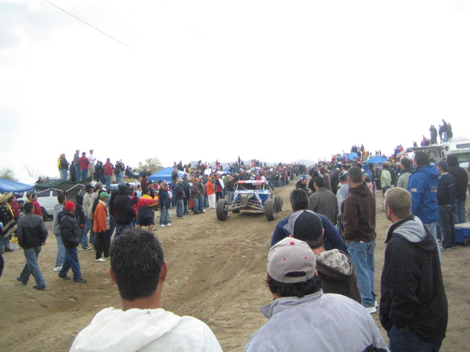 Yellow off-road buggy driving down a dirt course past spectators
