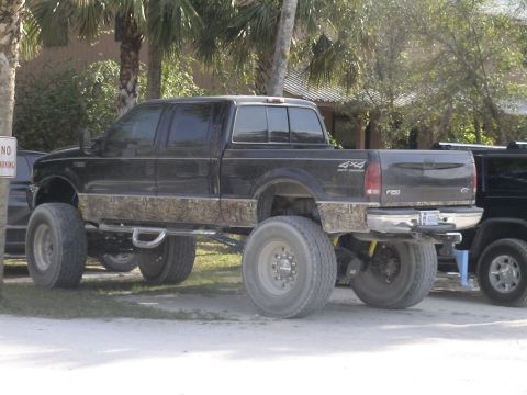 1993 Ford C-350 (Centurion Conversions) - A heavily modified black Ford F-250 Super Duty pickup truck is parked outdoors with large tires and a lifted suspension.