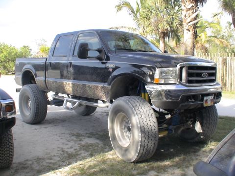 1993 Ford C-350 (Centurion Conversions) - A black lifted Ford F-250 truck with oversized tires and camouflage trim is parked on a dirt lot.