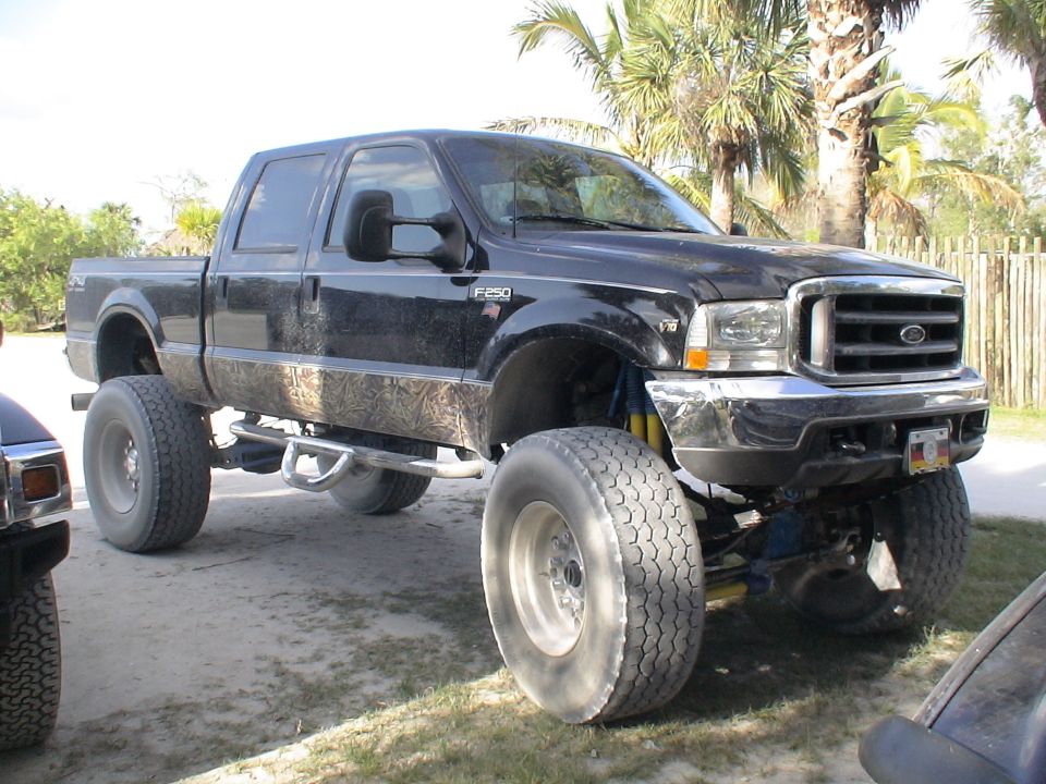 Lifted black Ford F-250 crew cab on oversized tires with yellow shocks, parked among palms