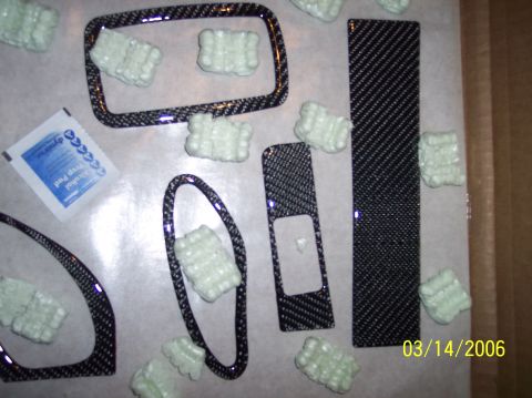 1995 Ford Probe - Carbon fiber interior trim pieces, likely for a car's dashboard, are laid out with packing peanuts and an alcohol wipe.