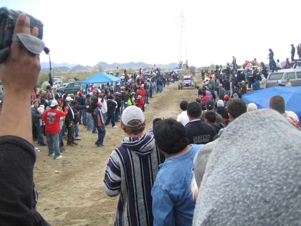 Spectator films an off-road buggy on a long dirt course lined with crowds