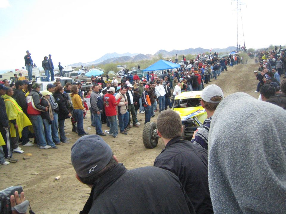 Yellow off-road buggy kicks up sand on a course lined with spectators