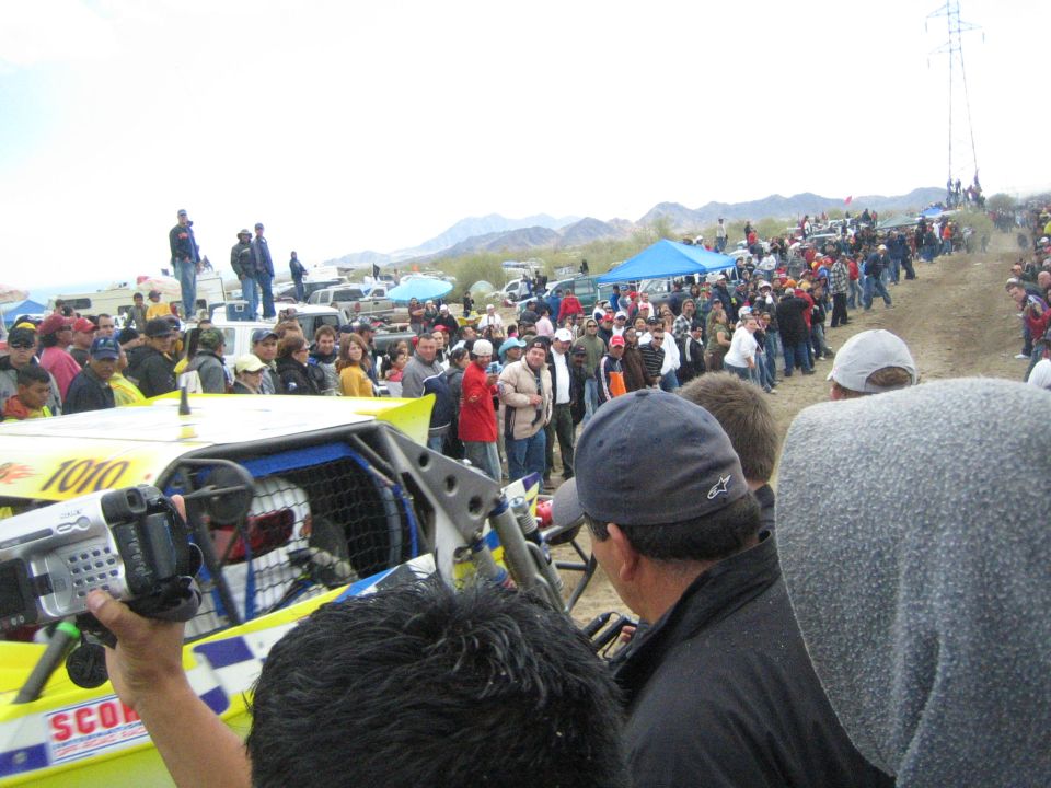 Yellow off-road buggy number 1010 with spectator filming on a dirt course