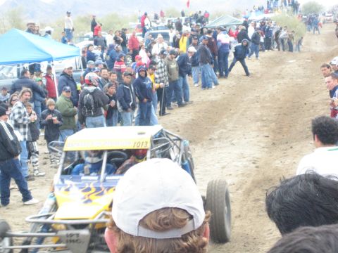 1990 Ford Bronco - yellow tube-frame off-road buggy marked 1013 runs a sandy course flanked by large crowds of spectators.